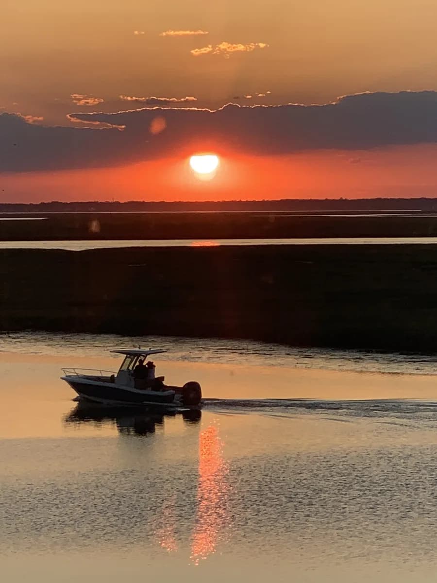 A center-console boat crossing the channel at sunset, the marsh behind it in silhouette